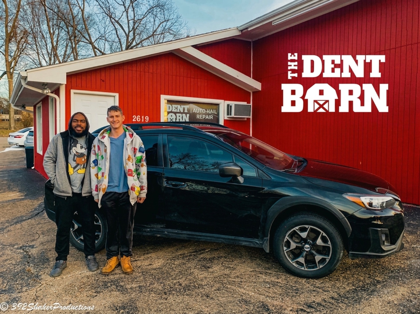 The front of the red Dent Barn building with a customer car parked at the door