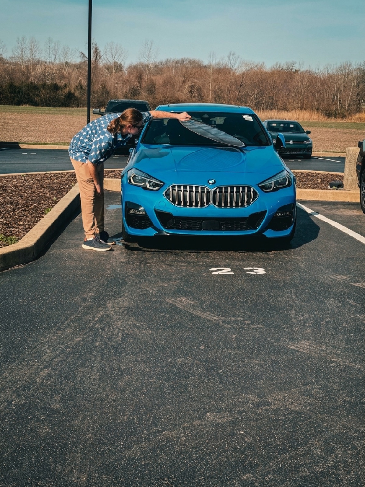A person bent down sighting along a car hood to look for hail dents