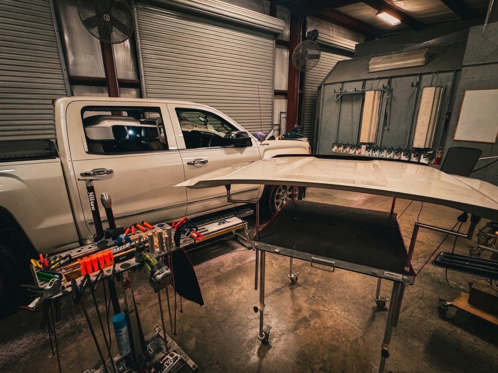 A hood on a paintless dent repair table beside the truck it came off
